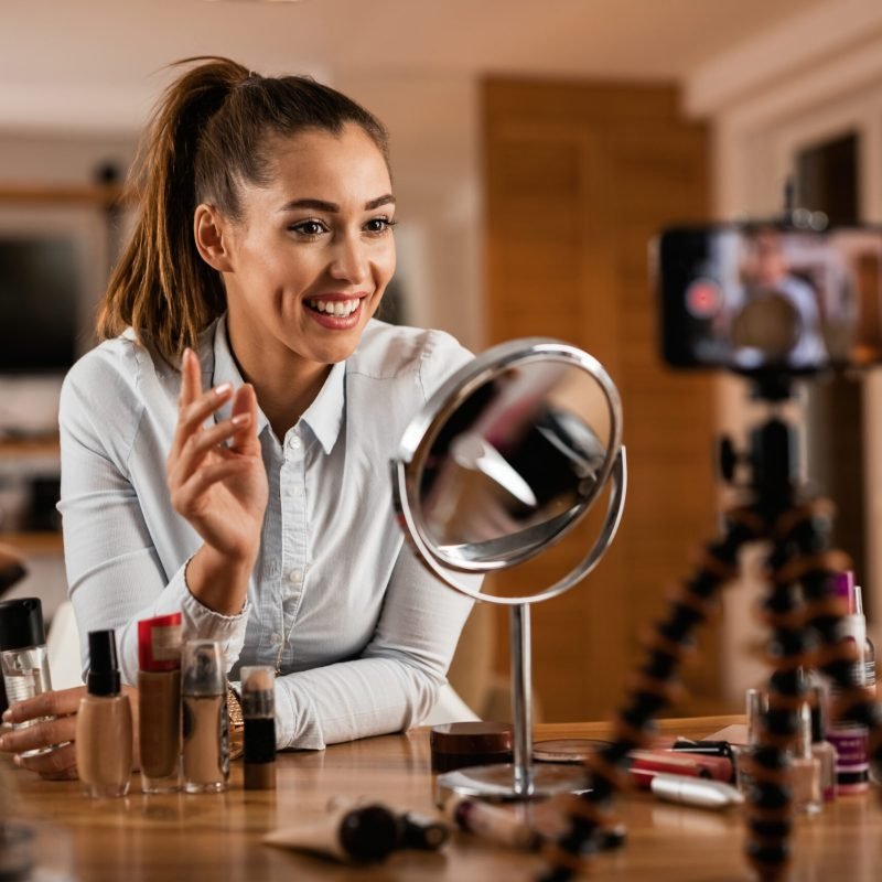 Smiling female influencer talking about beauty products while vlogging from home.